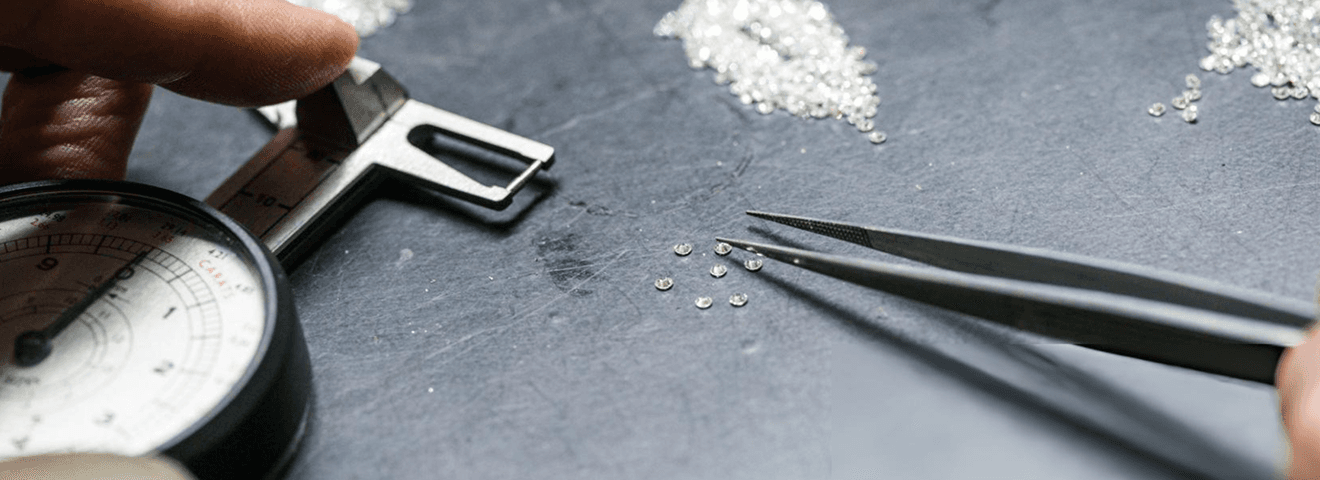 Close-up of small diamonds being sorted and measured with precision tools on a dark surface
